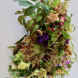 Floral arrangement with purple and apricot colored flowers and textural greenery